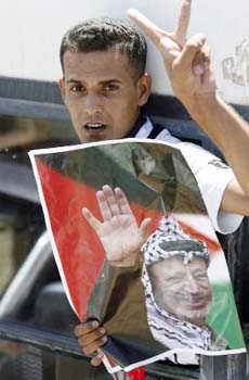 A released Palestinian prisoner, riding aboard a bus, gestures as he holds a poster of the late Palestinian leader Yasser Arafat at the Beituniya checkpoint near the West Bank city of Ramallah