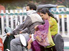 A woman riding pillion tries to shield her baby with dupatta from the showers in Ludhiana on Tuesday.