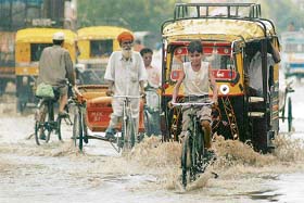 Commuters make their way along a waterlogged street during a heavy downpour of monsoon in Amritsar