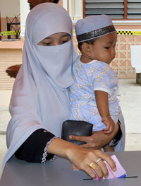 A veiled Thai Muslim voter drops a ballot paper into 