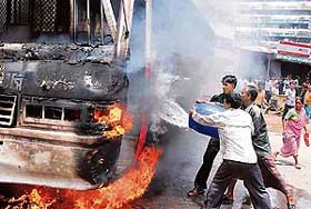 Shopkeepers try to control fire set on a bus during a protest to demand an end to emergency rule near the Dhaka University campus in Dhaka, Bangladesh