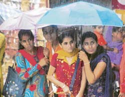 College students huddle under umbrellas near the post office bus stop at Dharamsala during a downpour