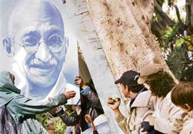 People in a park watch as a protester puts up a poster of Mahatma Gandhi in Sydney