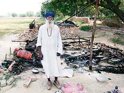 Chowkidar Atma Singh stands guard to the burnt hut.