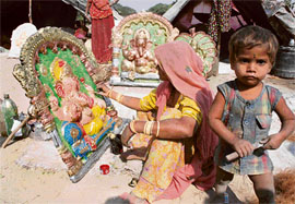 A woman gives finishing touches to an idol of Lord Ganesha in Karnal a few days before Diwali as her child plays near her.