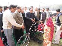 Irrigation and PWD minister Ajay Singh Yadav gives a tricycle to a disabled child at a World Disabled Day function at Rewari on Monday.