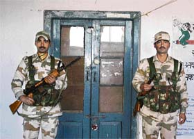 Two security personnel stand guard outside a room where EVMs have been stored at Palampur