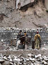 Labourers from Pakistan-occupied Kashmir clearing landslides as a Pakistani Ranger stands guard near Aman Saatu Bridge, connecting this part of the bridge with PoK at Kaman post, 118 km from Srinagar. Kaman Saatu was damaged in an earthquake in 2005. Repair works on the road are still continuing.