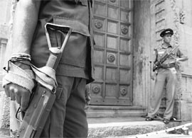 A Lankan soldier (left) and a policeman stand guard at the entrance to the temple where prominent Sri Lankan opposition Tamil parliamentarian T. Maheshweran was assassinated in Colombo on Tuesday.