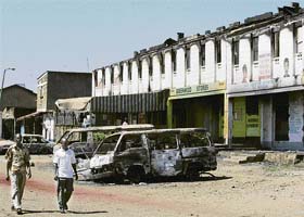 People walk past burnt vehicles and shops in Nairobi's Kibera slum