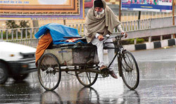 HIS CROSS: An old man looks for shelter for his family, under the tarpaulin, during rain in Mohali 