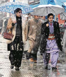 Two Kashmiri women with umbrellas walk in a market during a fresh spell of snowfall in Srinagar