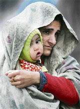 A woman protects her tender child, pulling a shawl over the head, on a cold rainy day in Jammu