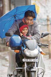 Under his fathers umbrella: A man takes his son on a motorcycle in rain in Amritsar on Thursday.