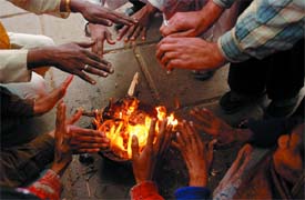 People warm themselves with firewood as temperature goes down in the Capital on Sunday