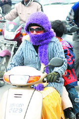 A woman covers her face with a muffler to save herself from cold while driving a scooter in Jalandhar