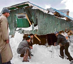 Kashmiri villagers look at a damaged house in Gulab Bagh village of Qazigund.