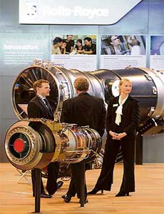 Exhibitors stand next to Rolls Royce engines for aircraft during the second day of the Singapore Airshow