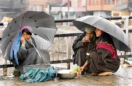 Amidst heavy rain, Kashmiri fisherwomen wait for customers on a footpath in Srinagar on Saturday. 