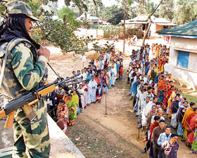 A soldier stands alert over voters as they queue to cast their votes at a polling centre in Mahanpur, some 35 km west of Agartala, on Saturday, during voting for state assembly elections.