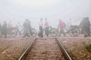 Commuters cross a railway track through dense fog close to the railway station in Amritsar on Sunday. 