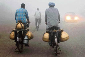 Milkmen go to deliver milk through thick fog in Amritsar on Saturday. Unseasonal heavy fog has disrupted rail and air traffic in northern India.