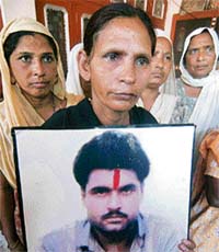 Sukhpreet Kaur holds a photograph of her husband Sarabjit Singh at their residence in Bhikhiwind village
