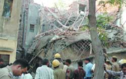 Fire personnel and people remove the debris of a collapsed house at Rohini in the Capital