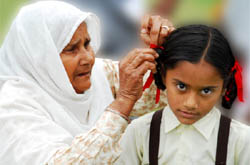 An old woman ties a ribbon to the plait of an orphan child at the Old Age Home in village Badal, in Muktsar district.