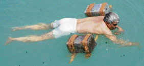 A trainer gives demonstration for swimming in a non-conventional manner with the help of a bamboo and empty tins.