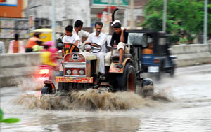 Riders watch as their tractor splashes water while crossing through a puddle on the Bathinda-Goniana road following rain on Sunday evening. 