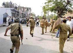Police personnel chasing a mob which resorted to stone-pelting after it was cane-charged. The mob was protesting against a demolition drive against illegal encroachments. 