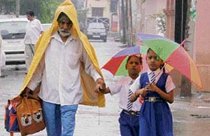 An elderly man escorts children to school amid showers in Ludhiana on Thursday.