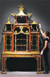 A Christies employee poses with a George II parcel-gilt padouk cabinet-on-stand attributed to Thomas Chippendale at Christies auction house in London