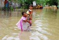 Aftermath: A woman (left) carrying a child tries to pass through the waist-deep water on the road