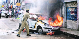 A policeman pours water to douse the flames after a car caught fire in Jammu on Friday. 