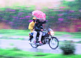 Two motorcycle riders struggle to adjust an umbrella during rain in Karnal