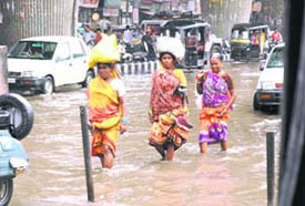 Commuters wade through a water-logged street opposite the railway station in Ludhiana on Sunday
