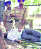 An undertrial who fell unconscious lying under a tree as policemen await help at the district courts complex in Chandigarh on Thursday.