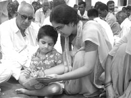 A teacher from Hardwar teaches a child how to write at a function of the yoga camp in Waryamkhera village of Abohar area.