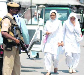 College girls walk past a CRPF jawan at Badshah Chowk in Srinagar