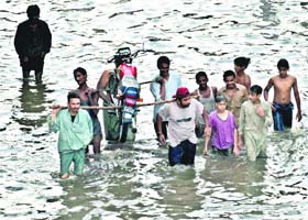 Pakistani youth carry a motorcycle as they cross a flooded street in Lahore