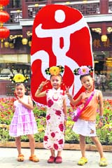 Young girls wearing traditional costumes pose for a photo in front of a logo of the 2008 Beijing Olympic Games in Shanghai
