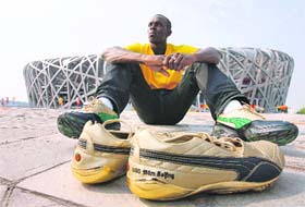 Current world record holder in the 100m sprint, Jamaica's Usain Bolt, sits behind the shoes he will be running in as he poses for a picture in front of the National Stadium, also known as the Bird's Nest, ahead of the Beijing 2008 Olympic Games