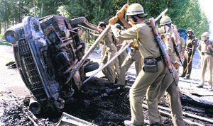 Policemen turn a damaged government vehicle, which was set afire during a protest demonstration at Bemina in Srinagar on Wednesday. 