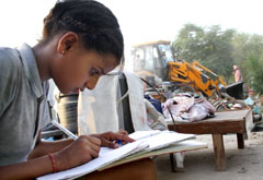 Simranjeet, a class V student of the Government Elementary School, concentrates on her studies while the PUDAs men and machinery (seen in background) bring her house down during a demolition drive carried out at Dhobiana Basti area of the Urban Estate in Bathinda on Tuesday.