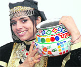 A girl seems to enjoy wearing a typical Himachali dress carrying a pitcher on her shoulder.