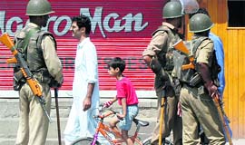 A boy rides past CRPF personnel during the curfew relaxation in Srinagar on Thursday. 