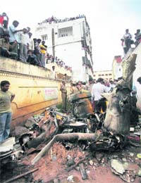 The police and local people watch the wreckage of the training plane of the Andhra Pradesh Aviation Academy that crashed at Sanath Nagar in Hyderabad