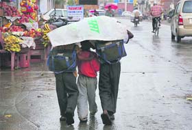 Three schoolchildren take shelter under a polythene sheet during rain in Karnal